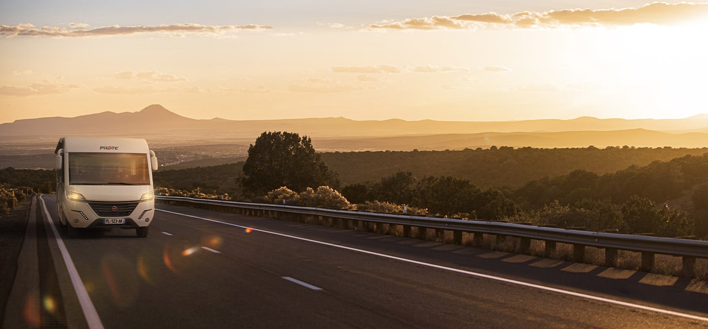 Camping-car intégral Pilote sur une longue route, à la lumière de fin de journée.