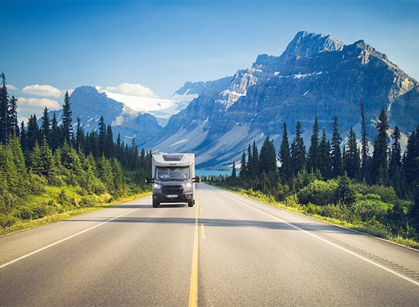 Camping-car profilé étroit Pilote roulant sur une route de montagne, la montagne et un lac turquoise au loin.