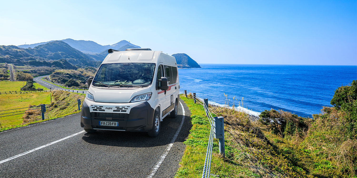 Vue de face d'un fourgon aménagé Pilote roulant au bord de mer