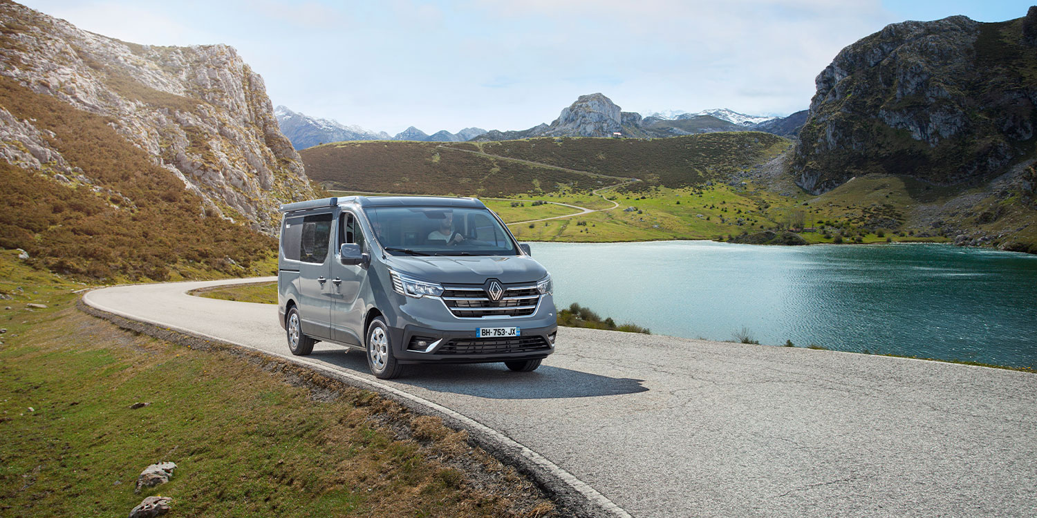 Van aménagé Pilote roulant le long d'un lac dans un paysage montagneux