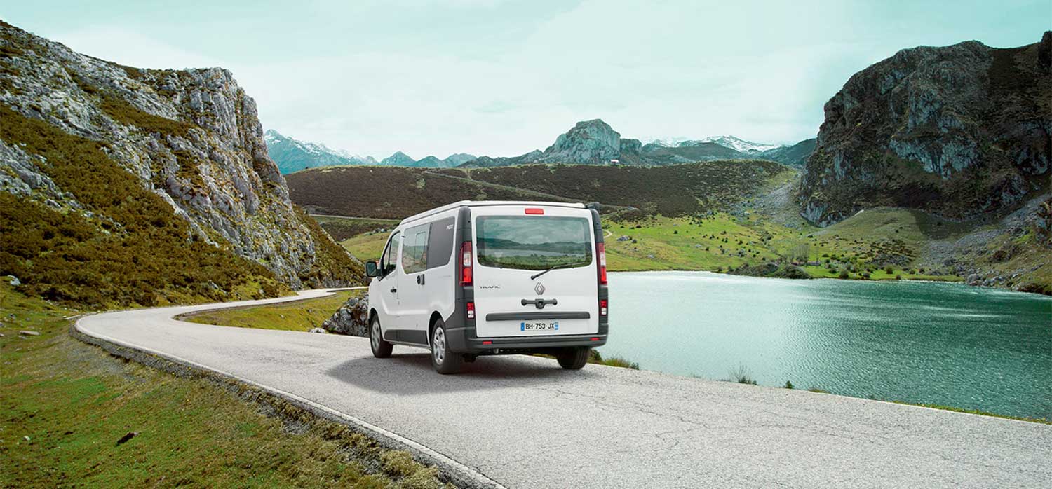 Van aménagé Pilote roulant au bord d'un lac en montagne.